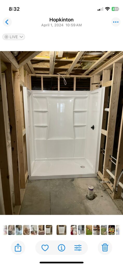 A newly installed white shower stall in a bathroom under construction with exposed wooden framing.