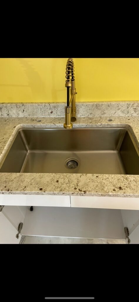 Modern kitchen sink with brass faucet and granite countertop.