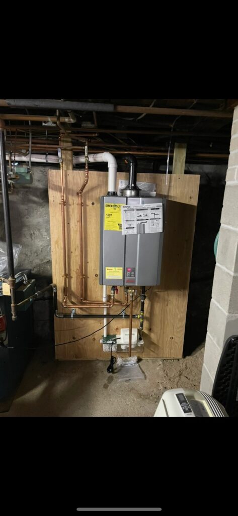 Tankless water heater installed on a wooden panel in a basement.
