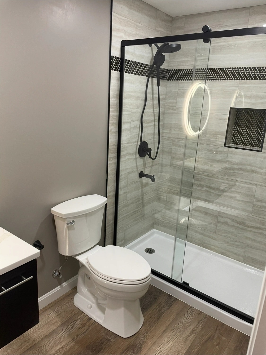 Remodeled bathroom with a tiled walk-in shower, black-framed glass door and a white toilet.